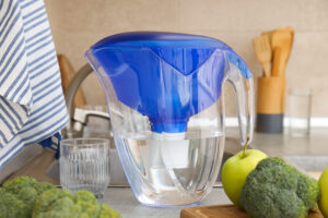 A water filter stands in the kitchen with fresh vegetables